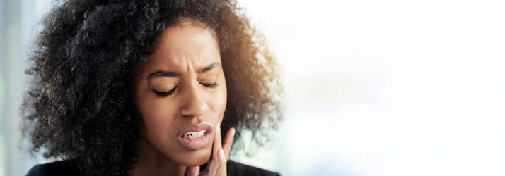 Person holding their face in discomfort, representing TMJ-related symptoms treated at Four Winds Chiropractic.