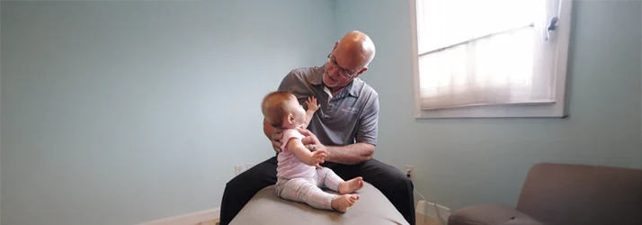 Dr. Jeff Tosch gently supporting an infant during a calm pediatric care session in a treatment room.